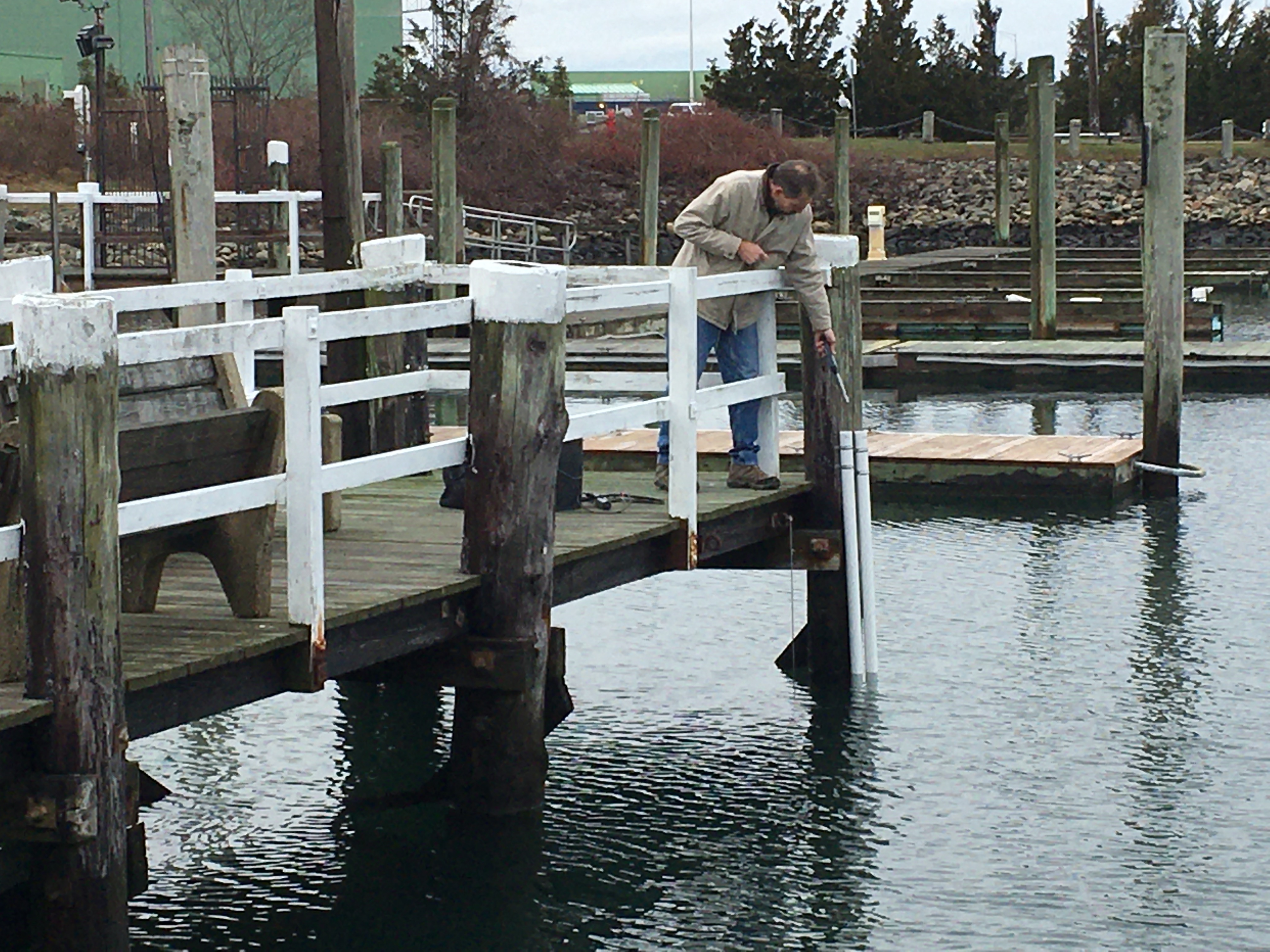 Person using a Bluetooth water level logger installed in a stilling well beside a dock